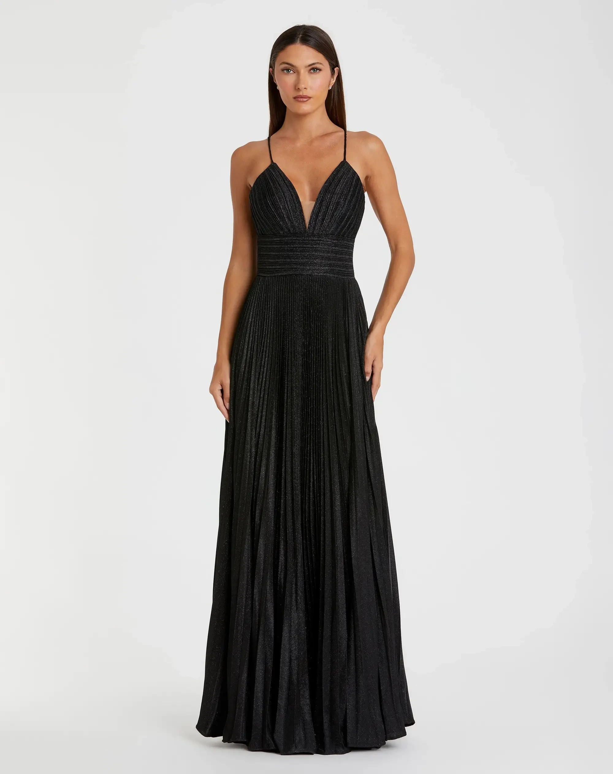 A woman in a black gown with a pleated design and thin straps, standing elegantly against a plain background.