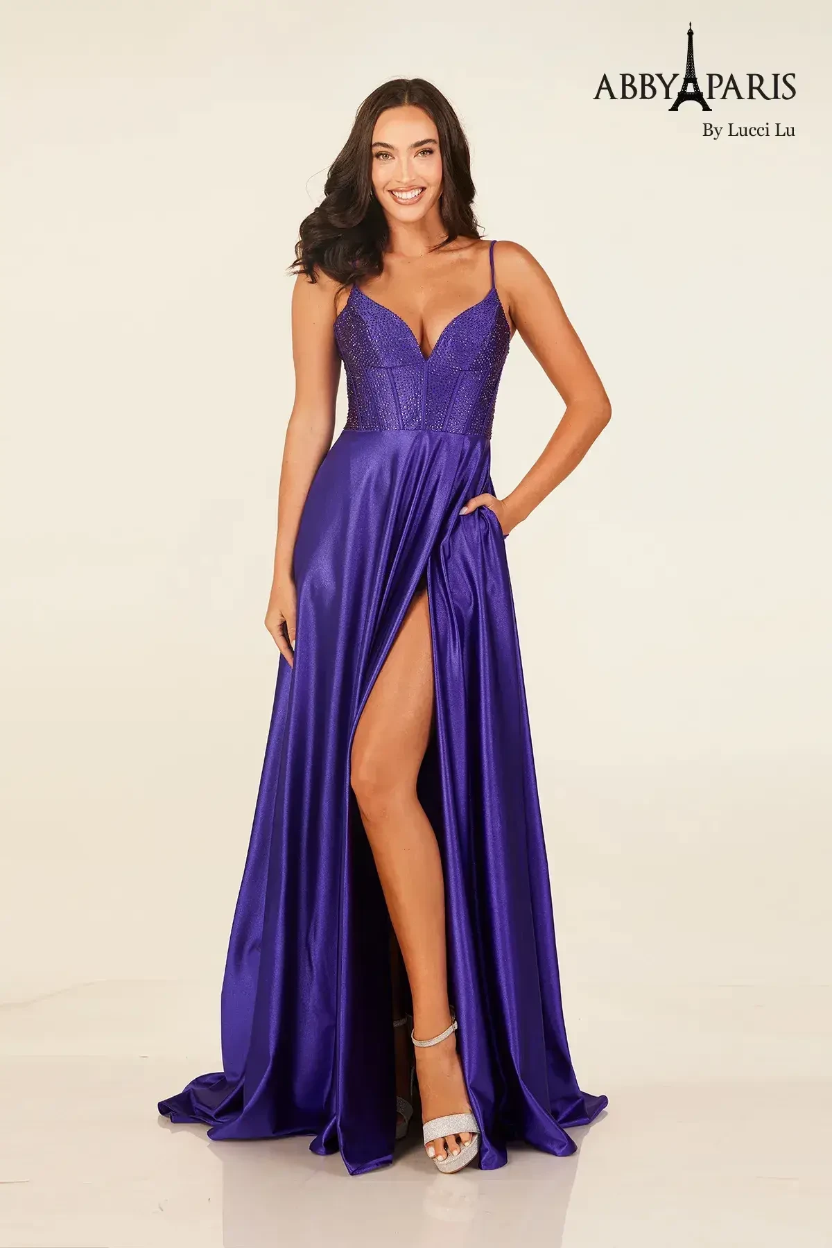A woman wearing a long, elegant purple dress with a slit on one side, posing confidently.